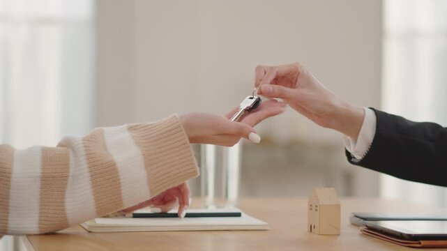 Close-up of a real estate agent in a black suit handing over house keys to a new homeowner.