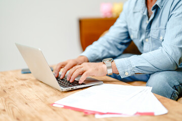 Individual working on a laptop at a wooden table in a modern and bright workspace during daylight...