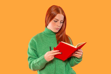 Young woman reads a book while dressed in green sweater against  orange background in a casual and...