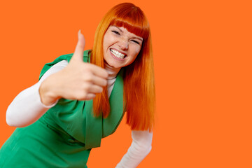 Brightly dressed woman gives a thumbs up against a vibrant orange backdrop in an indoor setting