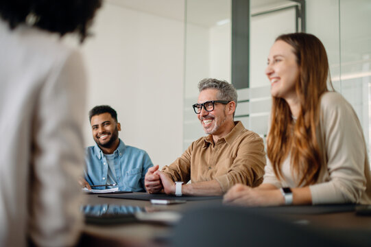 A diverse group of professionals in a business meeting, engaged in a conversation. The atmosphere is collaborative, with smiling faces and teamwork in a modern office.