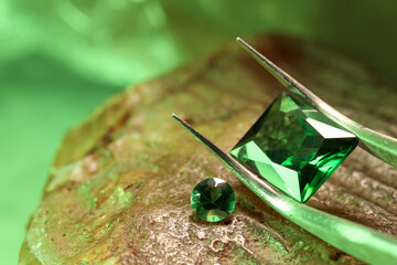 Tweezers with beautiful green gemstones on stone, closeup. Space for text