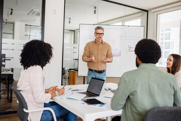 A professional business team discusses a strategic plan in a modern office. A middle-aged man...