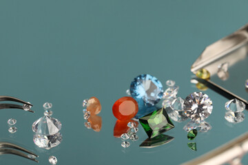 Beautiful colorful gemstones and tweezers on mirror surface, closeup