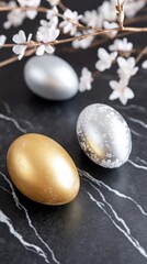 Golden and silver easter eggs on black marble surface with white flower branches