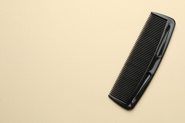 One black plastic comb on beige background, top view. Space for text