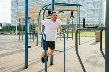 A man exercises energetically on parallel bars in an outdoor urban gym, enjoying a sunny day with a...
