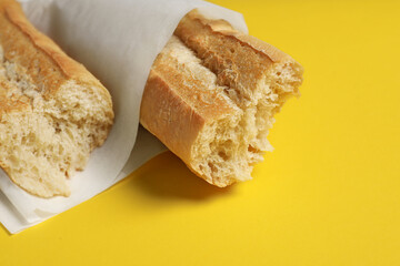 Paper bag with fresh baguette on yellow background, closeup. Space for text