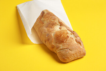 Paper bag with fresh baguette on yellow background, closeup