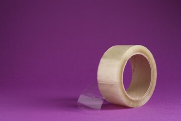 Roll of adhesive tape on violet background, space for text