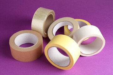 Rolls of different adhesive tapes on purple background, closeup