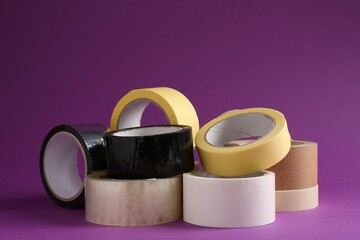 Rolls of different adhesive tapes on purple background