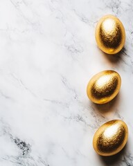 Obraz premium Three golden eggs arranged vertically on a white marble surface. The eggs shimmer against the cool background creating a luxurious feel