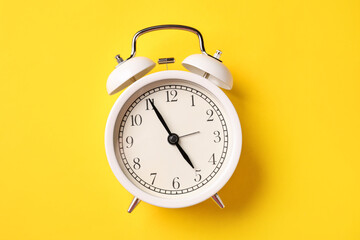 White alarm clock on yellow background, top view