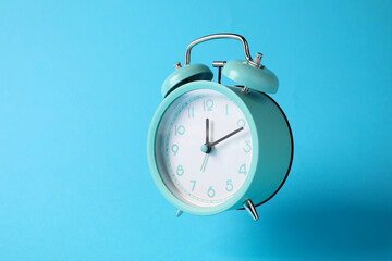 Turquoise alarm clock in air on light blue background