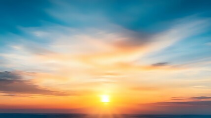 Obraz premium Dramatic sunset sky with vibrant orange and blue colors, soft wispy clouds creating ethereal atmosphere against glowing sun on horizon. Perfect for nature backgrounds.