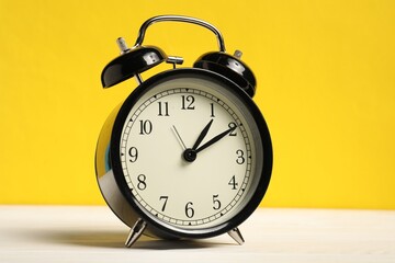 One black alarm clock on white wooden table against yellow background