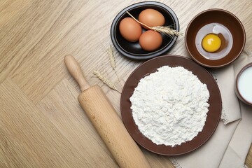 Rolling pin and ingredients for dough on wooden table, flat lay. Space for text