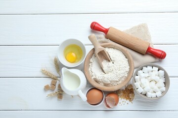 Rolling pin and ingredients for dough on white wooden table, flat lay. Space for text
