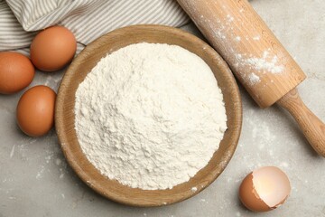 Rolling pin, flour and eggs on light grey background, flat lay