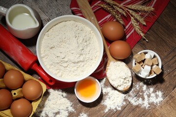 Rolling pin and ingredients for dough on wooden table, flat lay