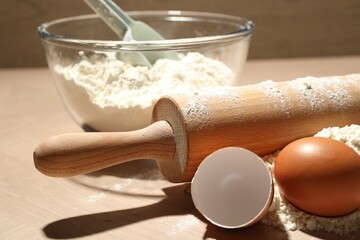 Rolling pin, flour and egg on wooden table, closeup