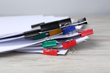 Binder clips with sheets of paper on wooden table, closeup