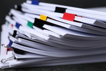 Colorful binder clips with sheets of paper on black background, closeup