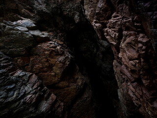 Rugged rock formations create a narrow passageway within a canyon, illuminated by faint light. The textures and colors of the stones reveal a hidden beauty, inviting exploration