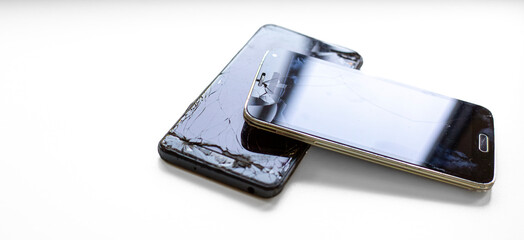 Two damaged smartphones with cracked screens stacked on a white surface, reflecting light. Concept of device repair, damage, and technology issues