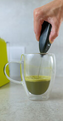 Frothing Matcha Tea with Handheld Whisk in Glass Mug vertical shot