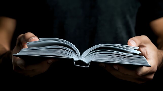 Female hands holding open book with white pages against dark background, dramatic lighting creates atmospheric mood for reading, education and literature concepts.