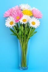 Fototapeta premium Vibrant pink, white, and yellow daisies in a clear glass vase against a light blue background. Close up view.