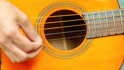 Fototapeta premium Detailed close-up of a musician's hand strumming the strings of a classic wooden acoustic guitar, showcasing the texture and craftsmanship.