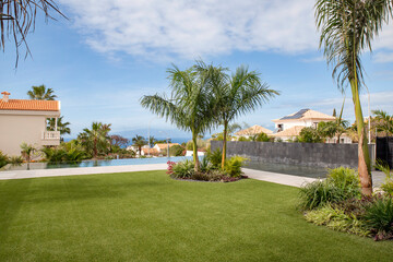 Beautiful garden surrounding a Spanish villa or a property featuring a lush green lawn, tropical...