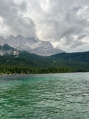 A peaceful mountain lake with crystal-clear water rests beneath stormy clouds. The mist-covered peaks and darkening sky add a sense of mystery to the scene.
