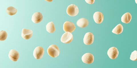 Floating macadamia nuts with soft, pale beige color on a light teal background