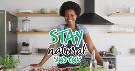 Image of stay natural text over happy biracial woman with apron at home