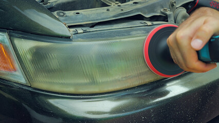 Close-up of a man using an electric drill with a polishing attachment to restore a cloudy and...