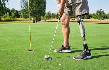 A determined golfer with a prosthetic leg focuses on putting a golf ball on a smooth green surface at a scenic golf course during the day