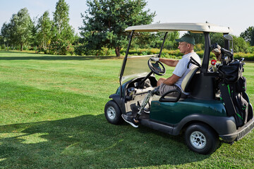 A golfer with a prosthetic leg drives a golf cart across a lush green course on a bright summer day, showcasing determination and skill