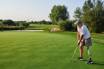 A golfer with a prosthetic leg prepares to putt on the green amidst the lush landscape and clear...
