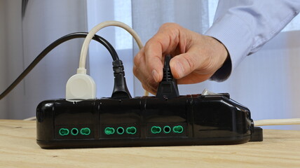 Cavi isolati collegati alla ciabatta nera, la mano dell'uomo inserisce i cavi elettrici con spina schuko nella ciabatta.