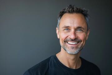 Fototapeta premium Portrait of a merry caucasian man in his 40s smiling at the camera while standing against soft gray background