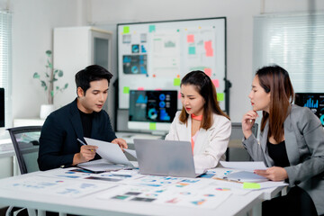 Diverse business team collaborating, reviewing financial data and marketing strategy on laptop in modern corporate workspace