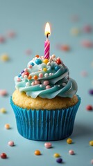 Colorful cupcake with blue frosting and a lit candle set against a pastel blue background for celebration