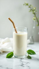 Glass of milk on a marble countertop with straw and mint leaf garnish.