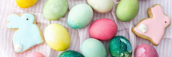 Multi-colored Easter eggs with decorative bunnies on a pink tablecloth, top view, Happy Easter holiday banner