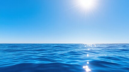 Fototapeta premium Bright sun over sparkling ocean horizon under clear blue sky.