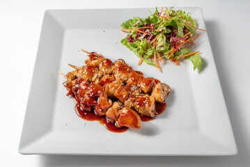 Traditional chicken yakitori, Grilled chicken skewers in Japanese sauce served on a plate with salad sauces on a white background